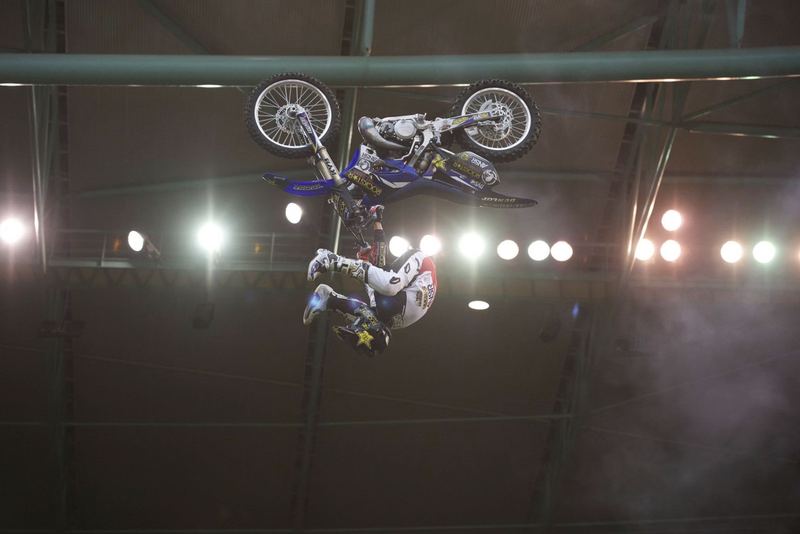 A freestyle motocross rider upside down above the stadium lights in an indoor arena