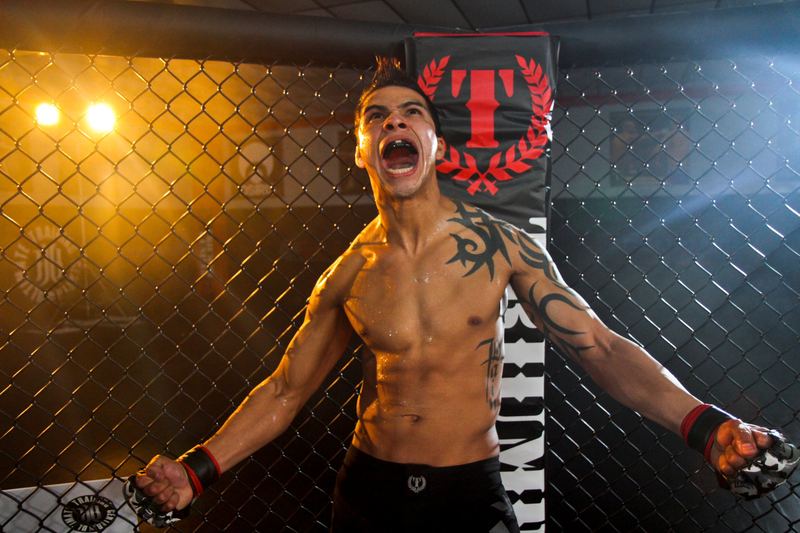 An MMA fighter roars with arms spread inside the cage
