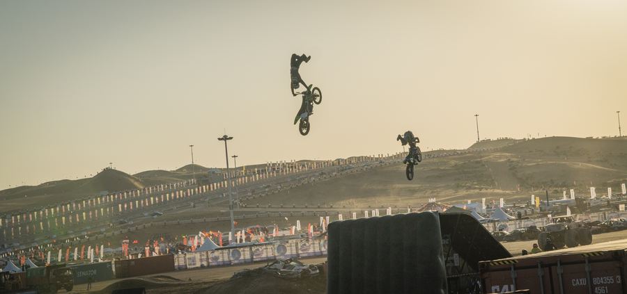 Two freestyle motocross riders upside down in the golden-hour sky over the Mongolian desert