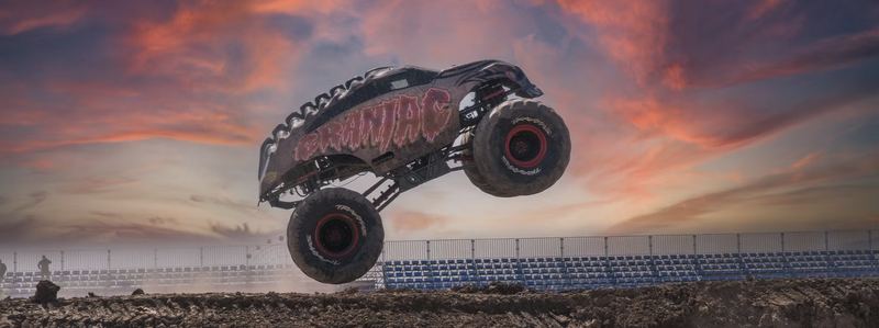A monster truck leaps through the air under a sunset sky