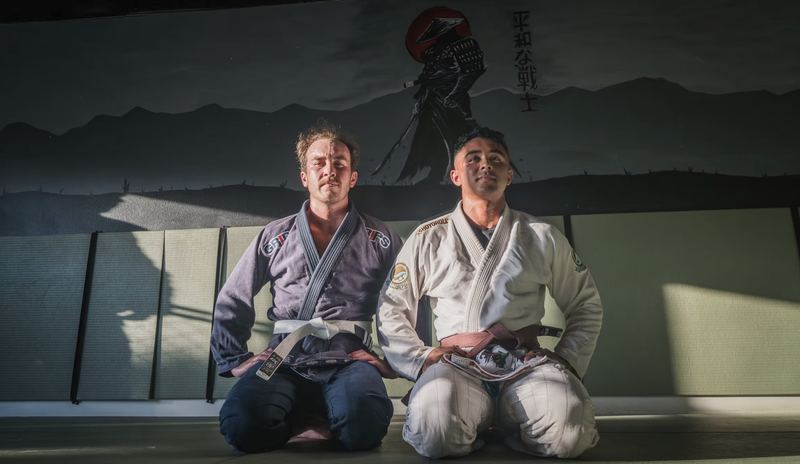 Two jiu-jitsu students kneeling on the mat in front of a samurai mural